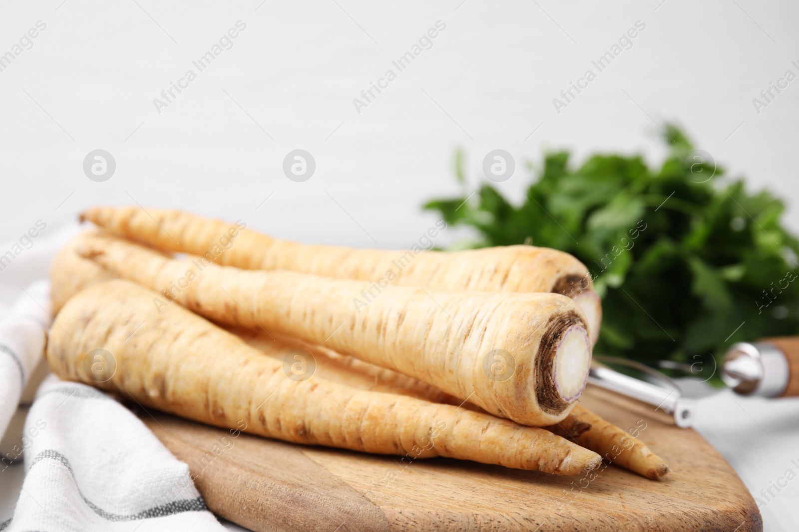 Photo of Whole raw parsley roots and fresh herb on white table, closeup