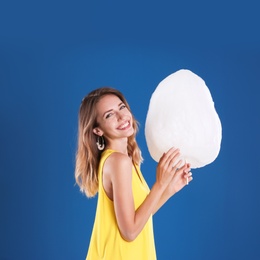 Photo of Happy young woman with cotton candy on blue background