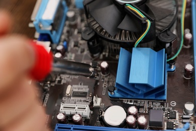 Photo of Technician repairing motherboard with soldering iron, closeup