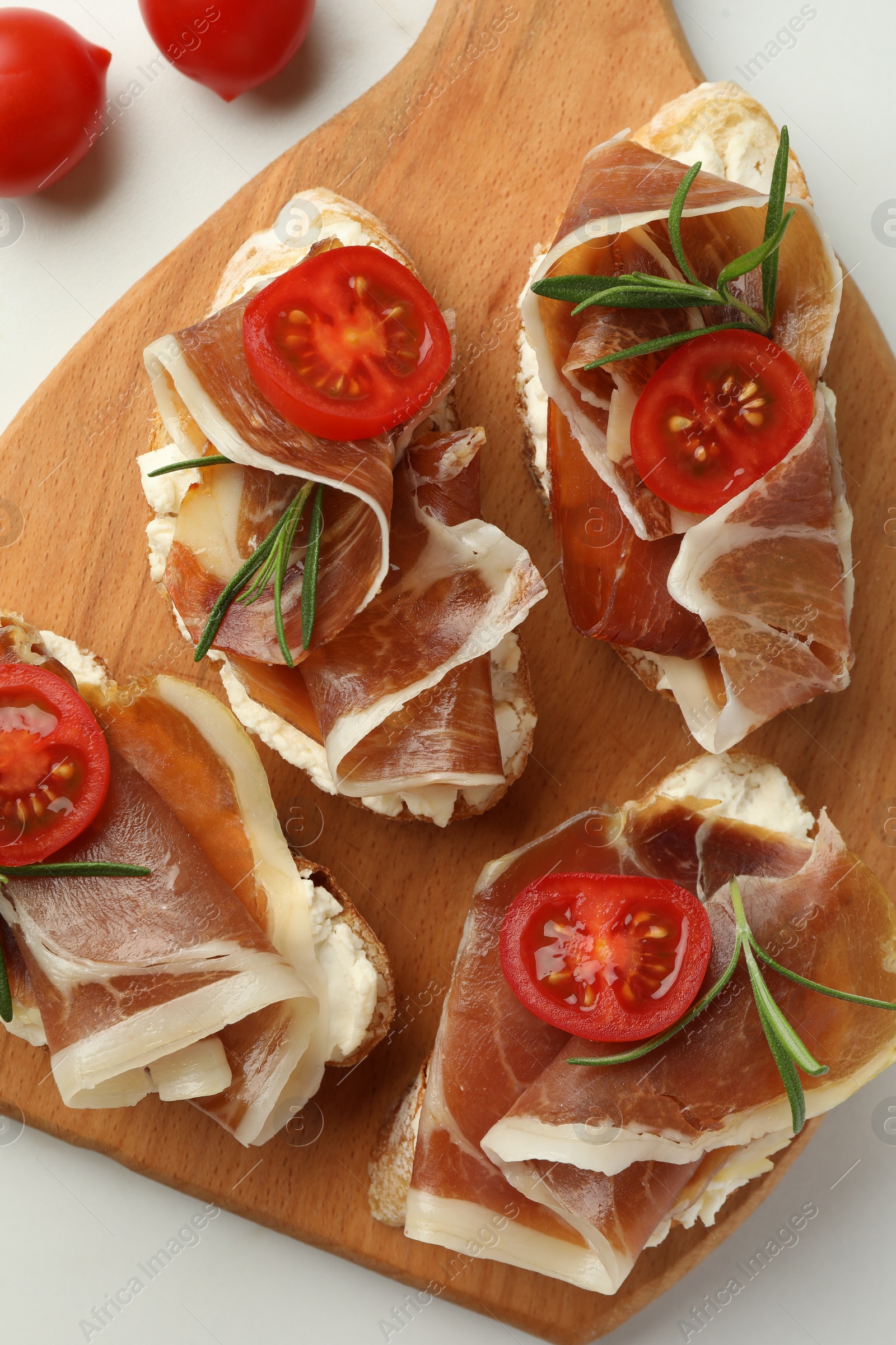 Photo of Tasty sandwiches with cured ham, rosemary and tomatoes on white table, top view