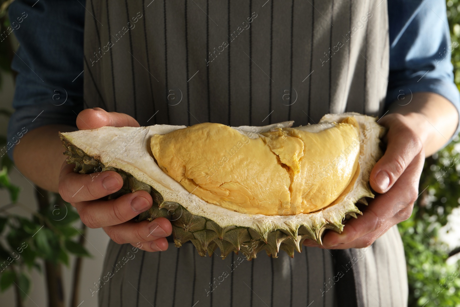 Photo of Woman holding piece of ripe durian on blurred background, closeup