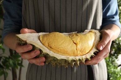 Woman holding piece of ripe durian on blurred background, closeup