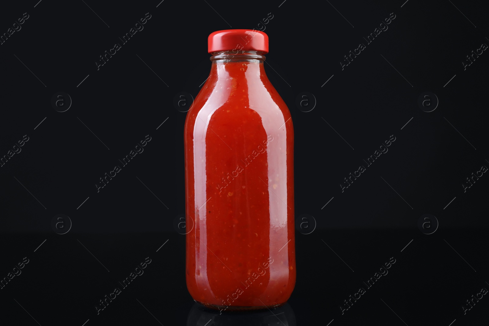 Photo of Spicy chili sauce in bottle on against dark background