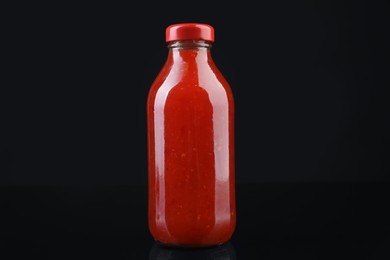 Photo of Spicy chili sauce in bottle on against dark background