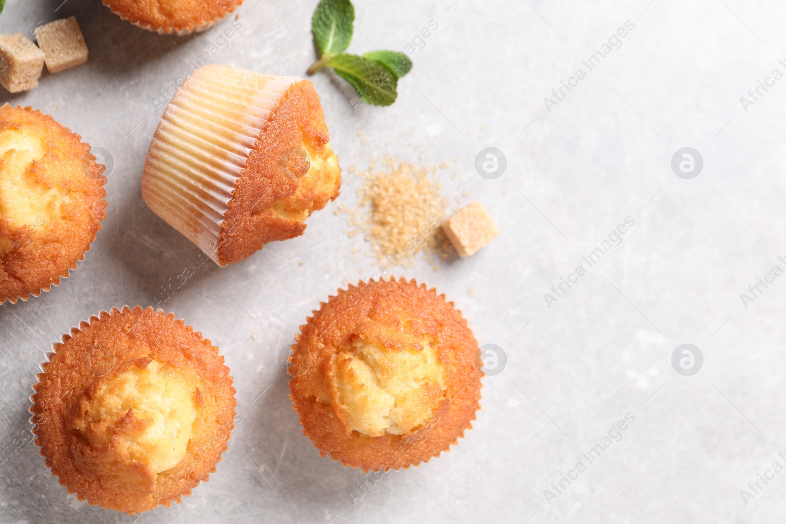 Photo of Delicious sweet muffins and brown sugar on light grey textured table, flat lay. Space for text