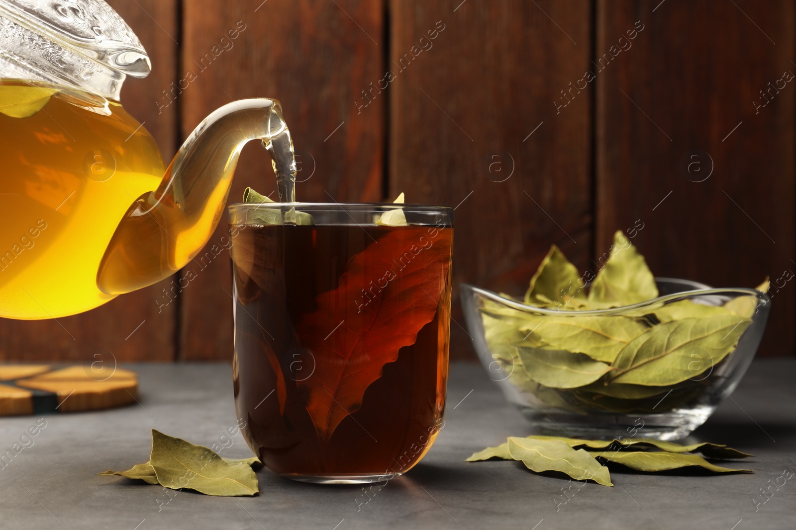 Photo of Pouring freshly brewed tea with bay leaves into cup on grey table