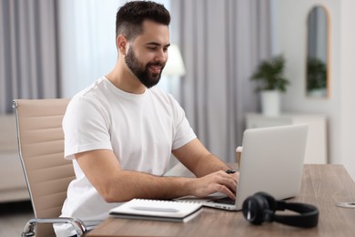 Photo of Young man watching webinar at table in room