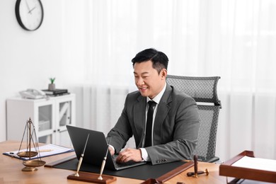 Happy notary working with laptop at wooden table in office