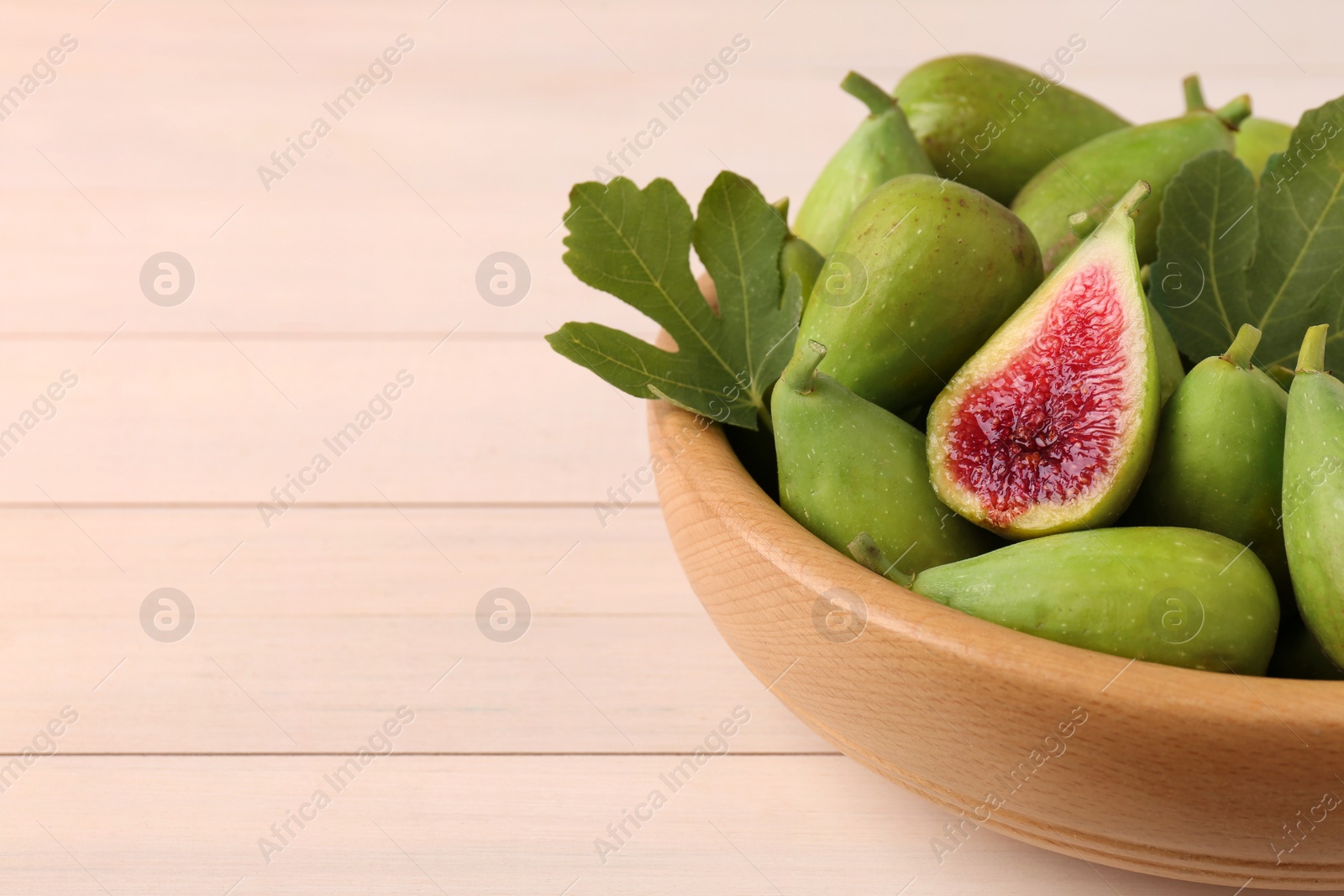 Photo of Cut and whole fresh green figs on white wooden table, closeup. Space for text