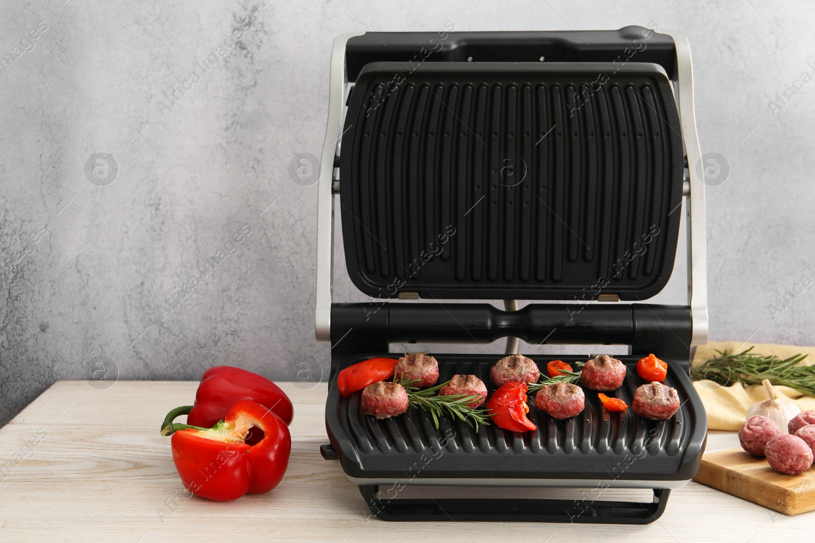 Photo of Electric grill with vegetables, meat balls and rosemary on wooden table