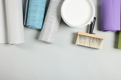 Photo of Different wallpaper rolls, brush and bucket with glue on light grey background, flat lay. Space for text