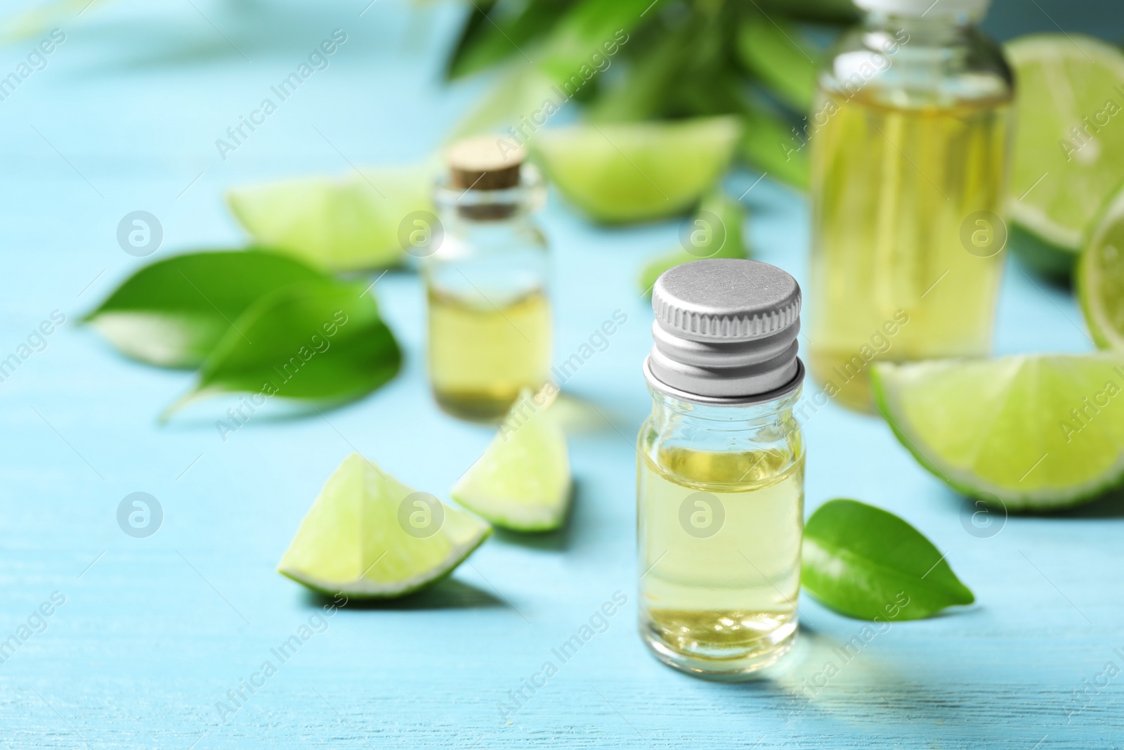 Photo of Lime essential oil and cut citrus fruits on light blue wooden table. Space for text