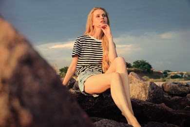 Photo of Beautiful young woman sitting on rocks outdoors