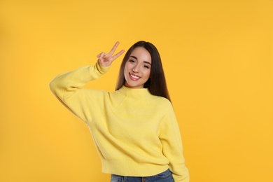 Beautiful young woman wearing warm sweater on yellow background