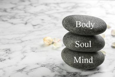 Photo of Stones with words MIND, BODY, SOUL on marble background, space for text. Zen lifestyle