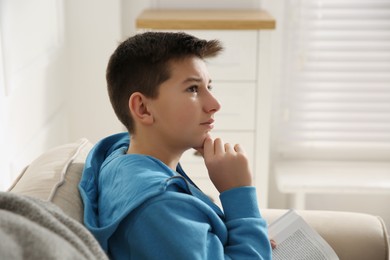 Thoughtful teenage boy with book on sofa at home