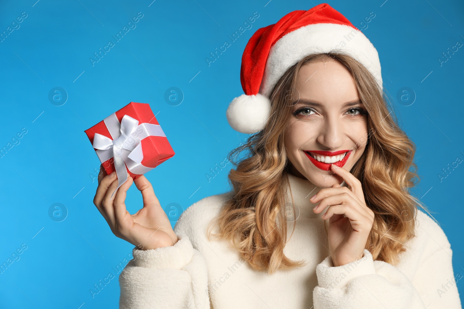 Photo of Happy young woman wearing Santa hat with Christmas gift on light blue background