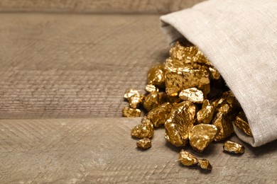 Overturned sack of gold nuggets on wooden table, space for text