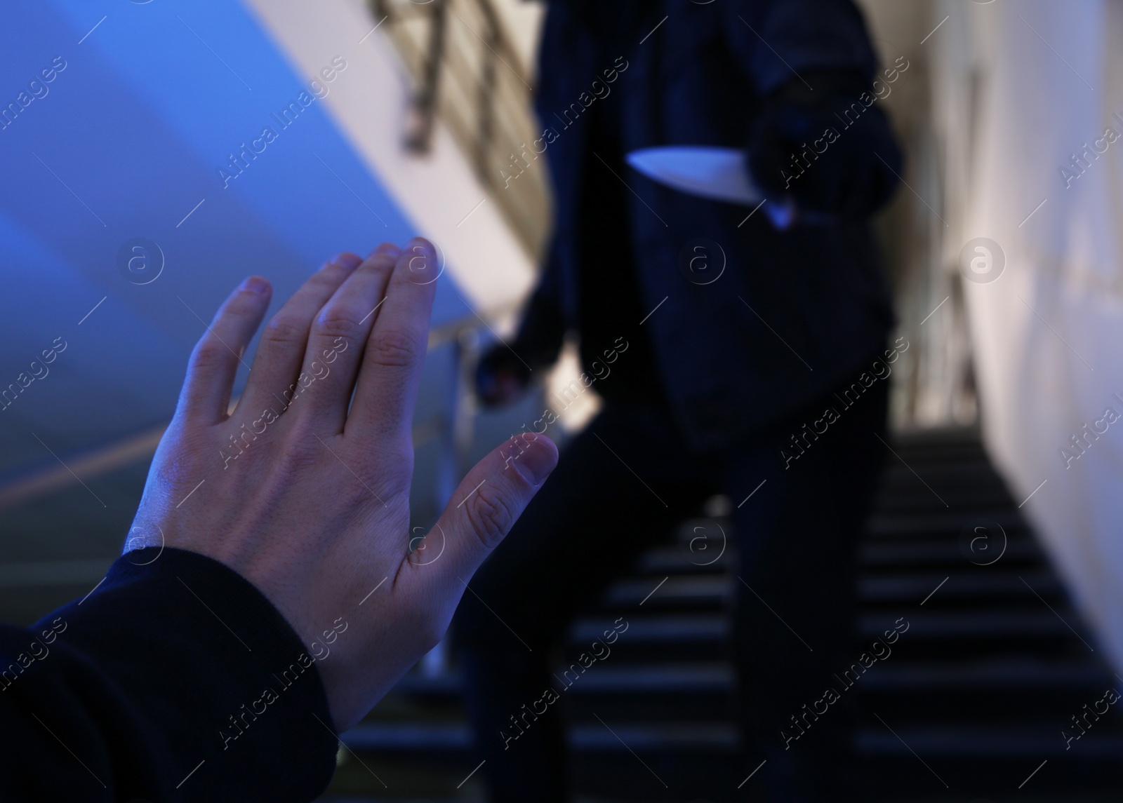 Photo of Criminal with knife attacking man on stairs indoors, closeup