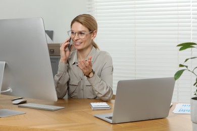 Photo of Professional accountant talking on phone while working at wooden desk in office