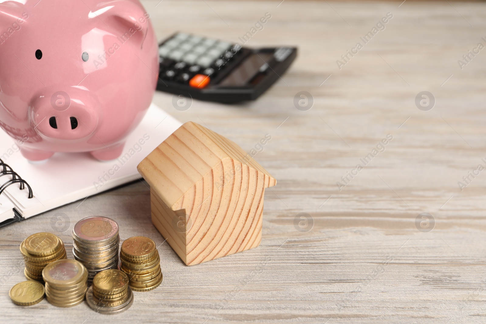 Photo of House model, piggy bank, stacked coins, notebook and calculator on wooden table, selective focus. Space for text