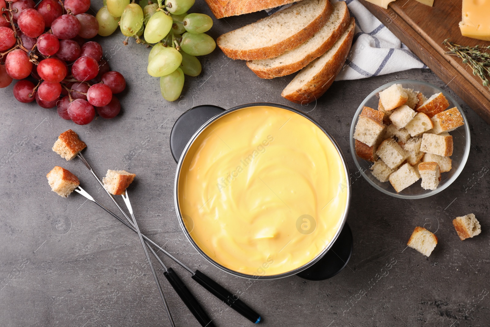 Photo of Flat lay composition with pot of delicious cheese fondue on gray table