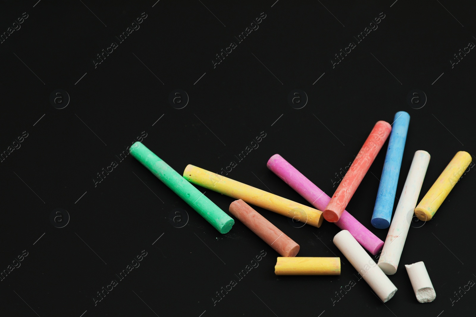 Photo of Colorful chalks on black board, above view. Space for text