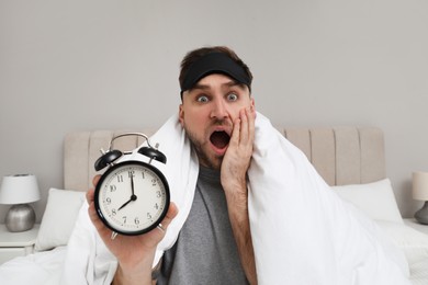 Photo of Emotional overslept man with alarm clock in bed. Being late concept