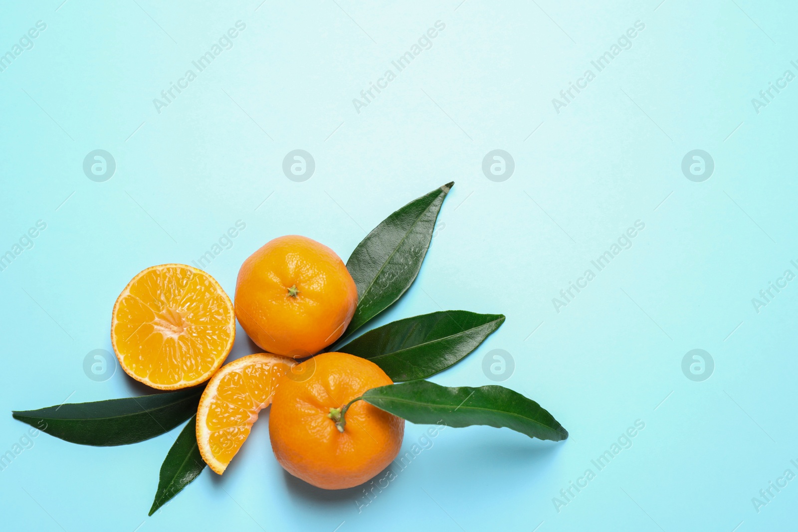 Photo of Flat lay composition with fresh ripe tangerines and leaves on light blue background. Citrus fruit