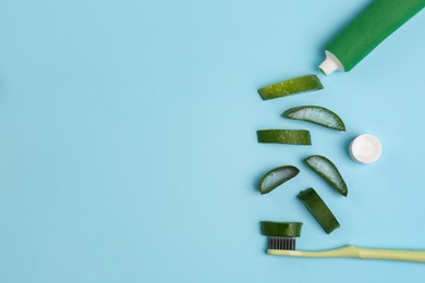 Tube of toothpaste, toothbrush and fresh cut aloe on light blue background, flat lay. Space for text