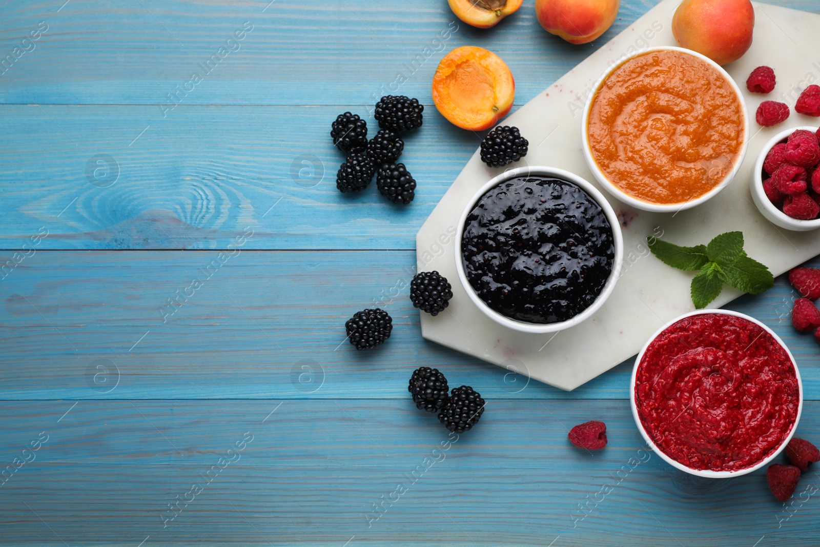 Photo of Different puree in bowls and fresh fruits on light blue wooden table, flat lay. Space for text