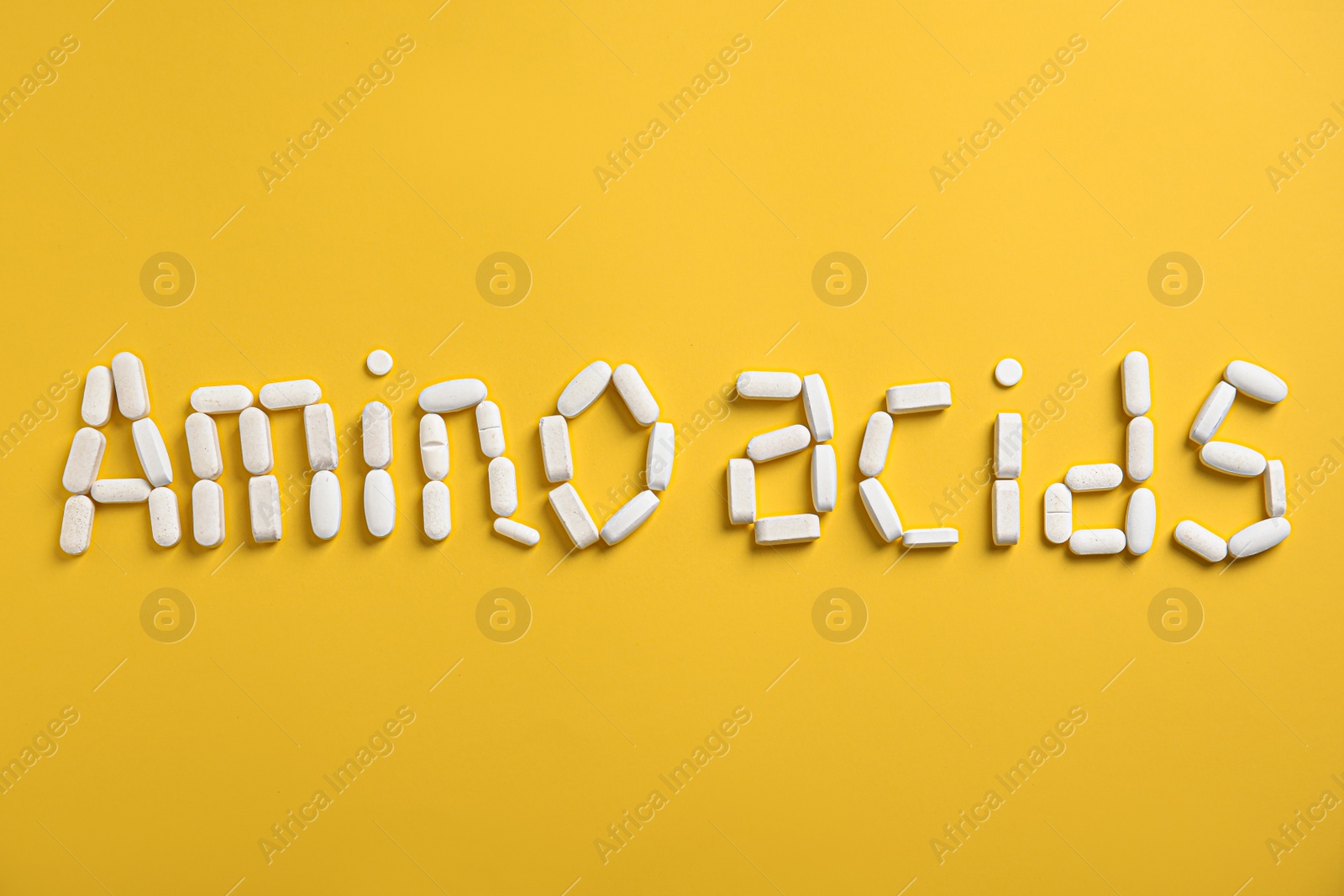 Photo of Words "AMINO ACIDS" made with pills on yellow background, flat lay