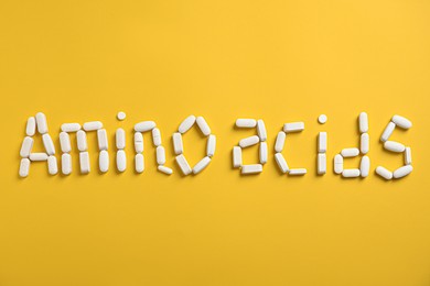 Words "AMINO ACIDS" made with pills on yellow background, flat lay