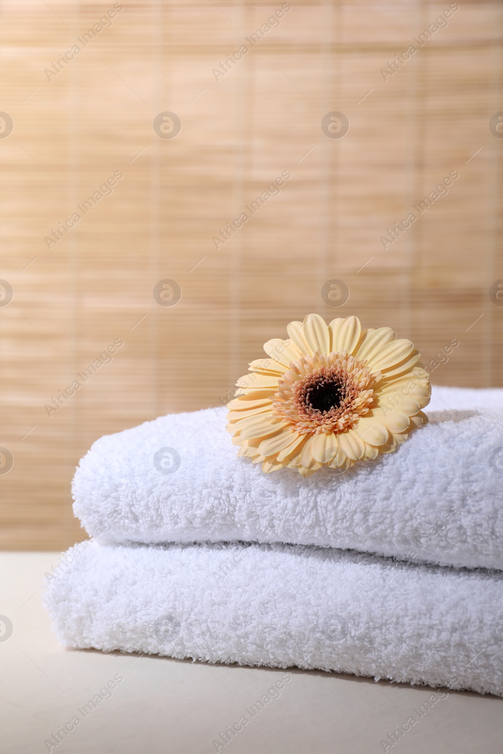 Photo of Stacked terry towels and flower on white table indoors, space for text