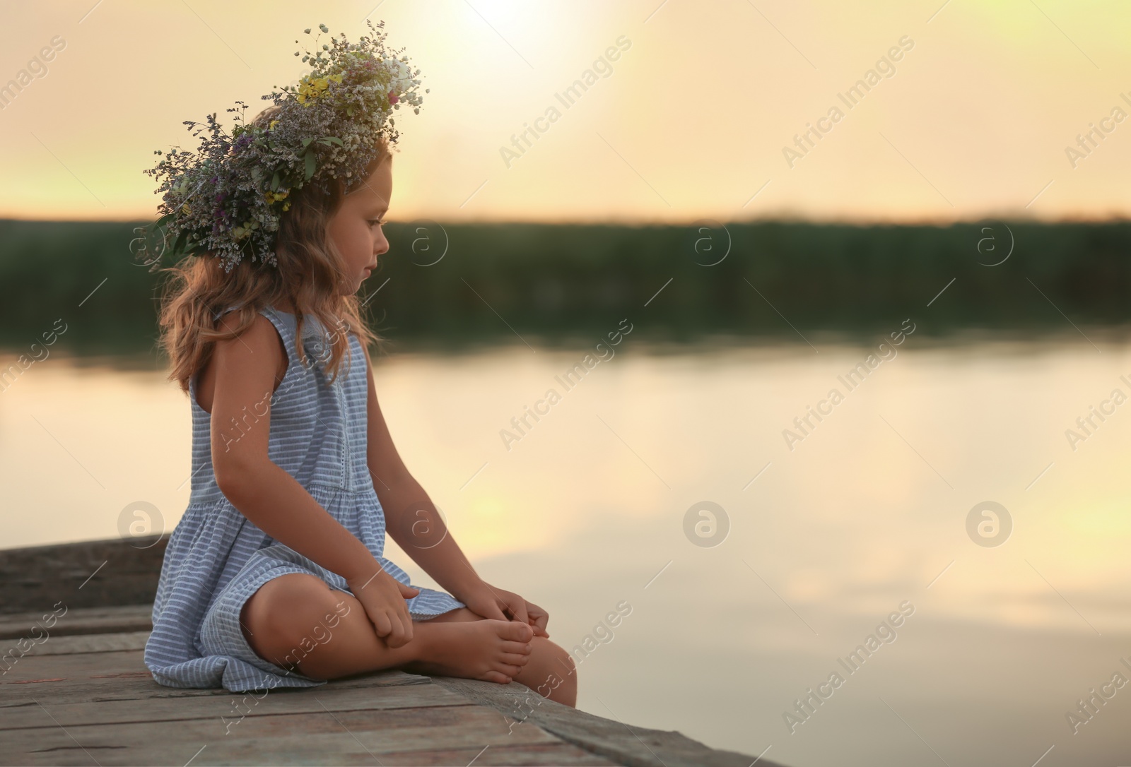 Photo of Cute little girl wearing wreath made of beautiful flowers on pier near river