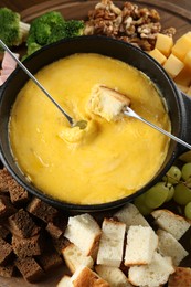 Photo of Fondue pot with melted cheese and different products on wooden table, top view