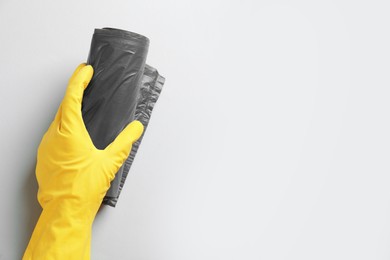 Photo of Janitor in rubber glove holding roll of grey garbage bags over light background, top view. Space for text