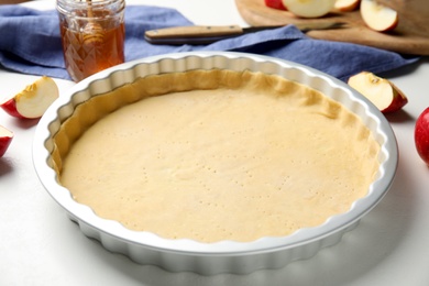 Photo of Baking dish with dough for traditional English apple pie on white table, closeup
