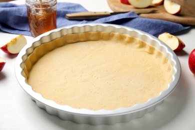 Baking dish with dough for traditional English apple pie on white table, closeup