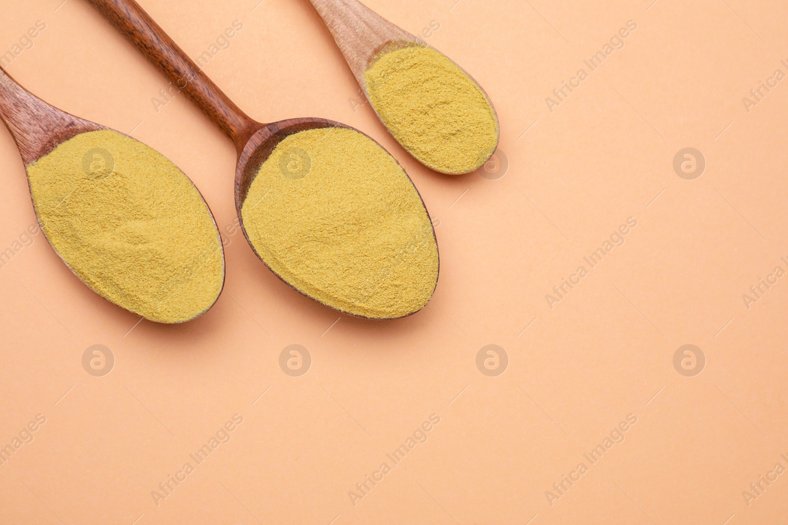 Photo of Different spoons with beer yeast powder on pale orange background, flat lay. Space for text