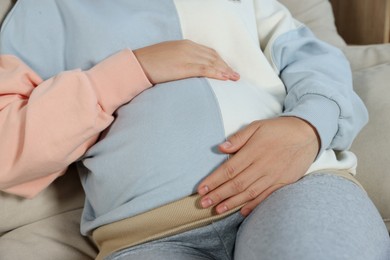 Pregnant woman touching belly indoors, closeup view