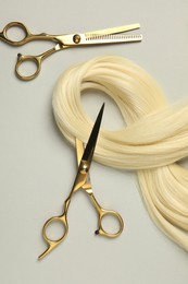 Professional hairdresser scissors with blonde hair strand on light grey background, flat lay