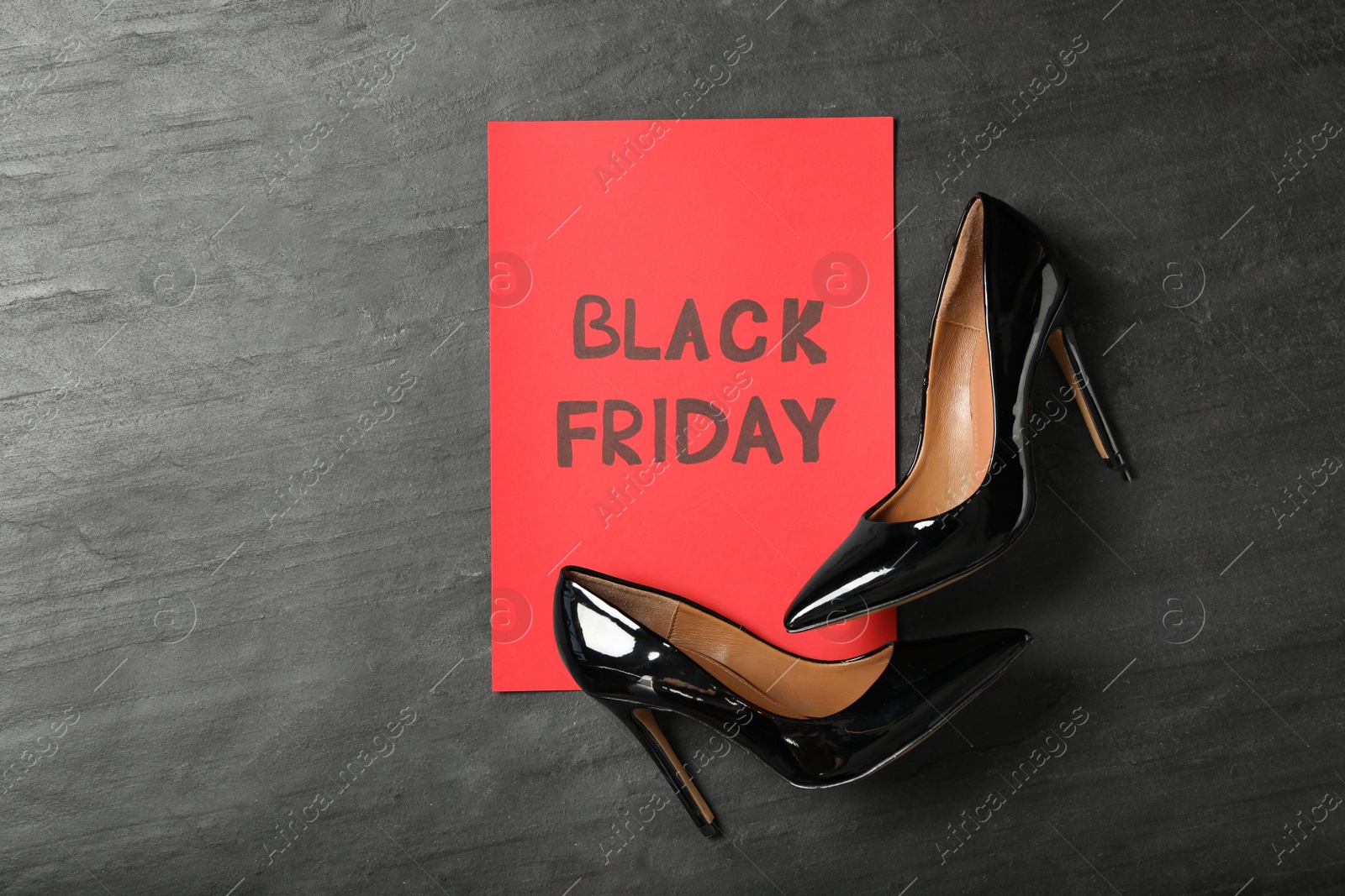 Photo of Elegant shoes and sheet of red paper with words Black Friday on dark background, flat lay. Space for text
