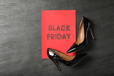 Elegant shoes and sheet of red paper with words Black Friday on dark background, flat lay. Space for text