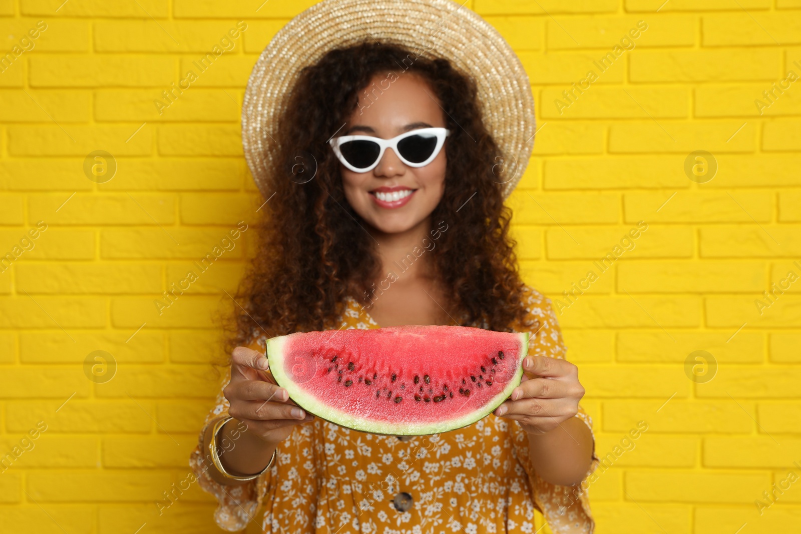 Photo of Beautiful young African-American woman with watermelon near yellow brick wall