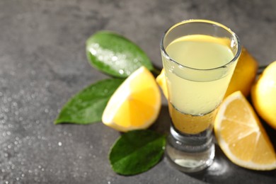 Photo of Tasty limoncello liqueur, lemons and green leaves on grey table, closeup. Space for text