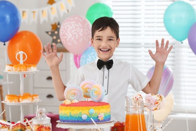 Photo of Happy boy at table with treats in room decorated for birthday party