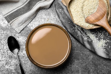 Photo of Tasty sesame paste, seeds and spoon on grey table, flat lay