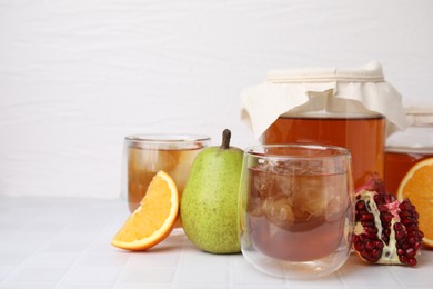 Tasty kombucha with ice cubes and fresh fruits on white tiled table, space for text