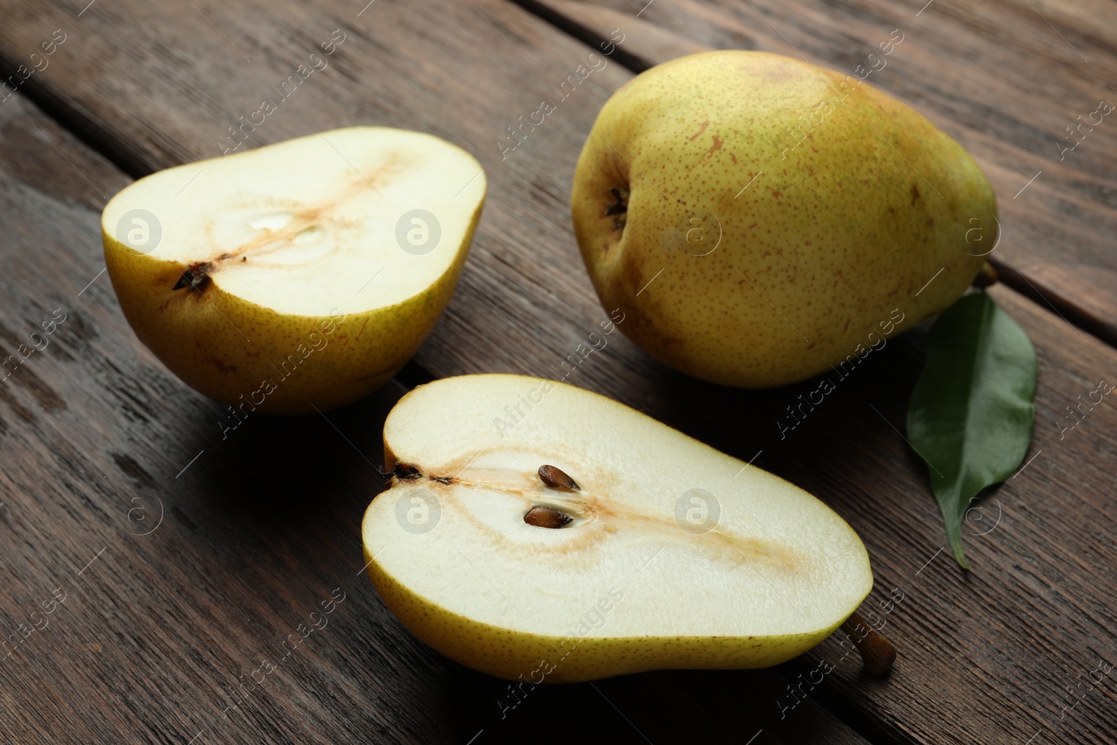 Photo of Whole and halves of tasty fresh pears on wooden table, closeup